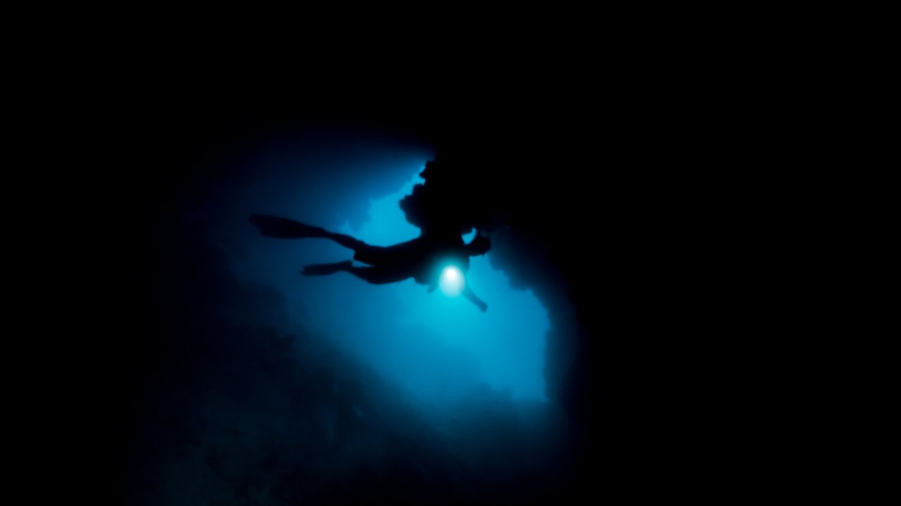 Diver silhouette with a dive light in a dark overhang